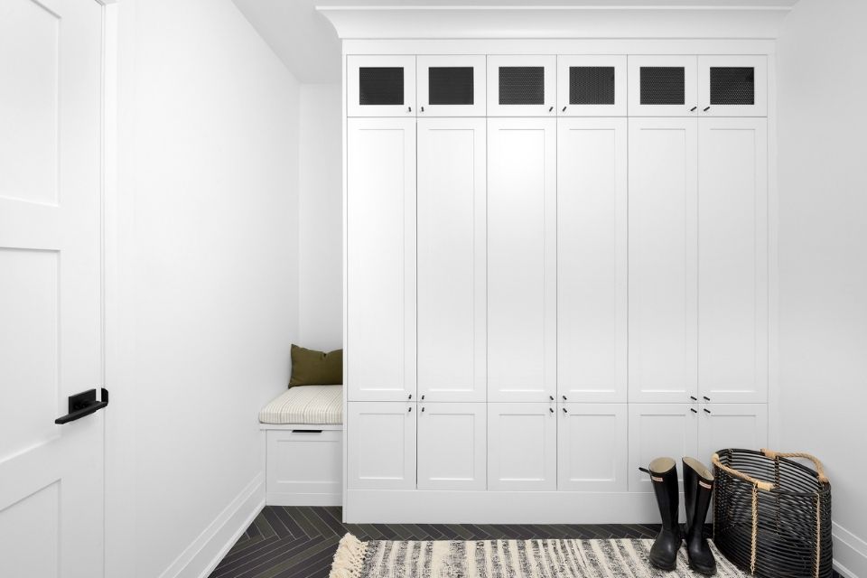 All white entryway with cabinet storage, black tile, and rug 