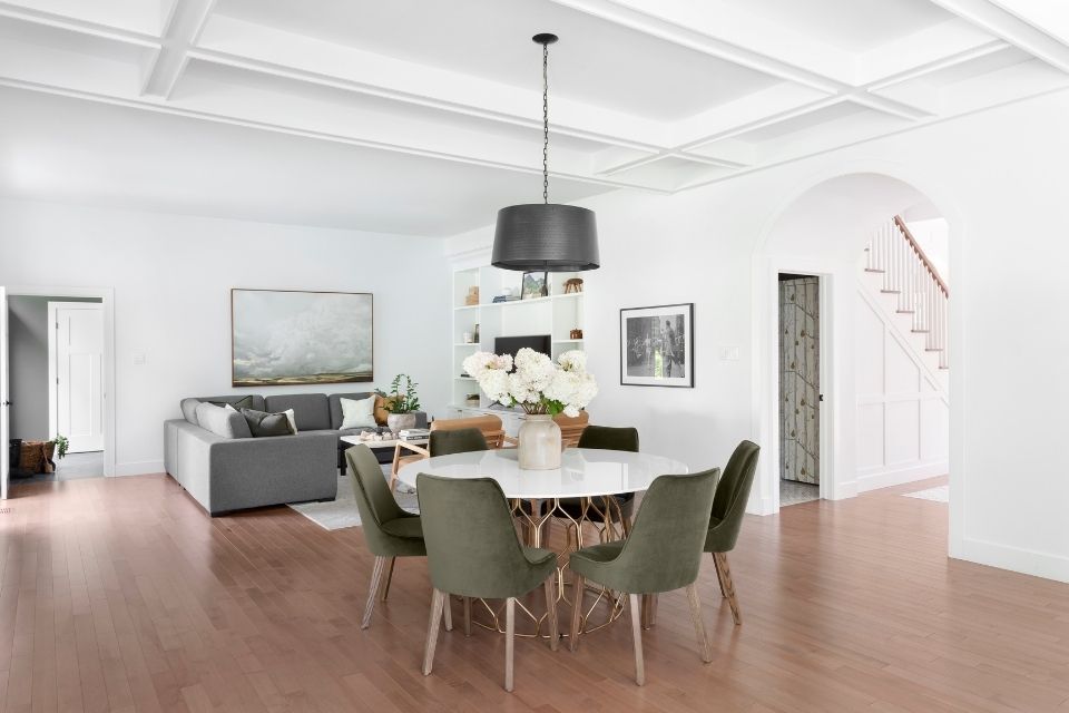 Open concept living and dining space with round table and sage green dining chairs