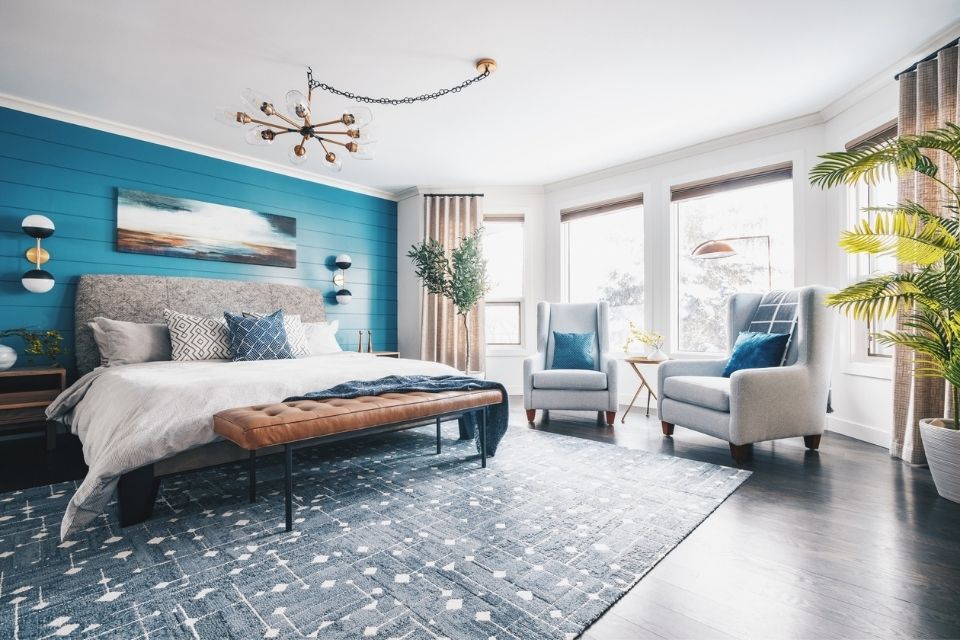 Blue accent wall in bedroom with seating included near window and blue area rug 