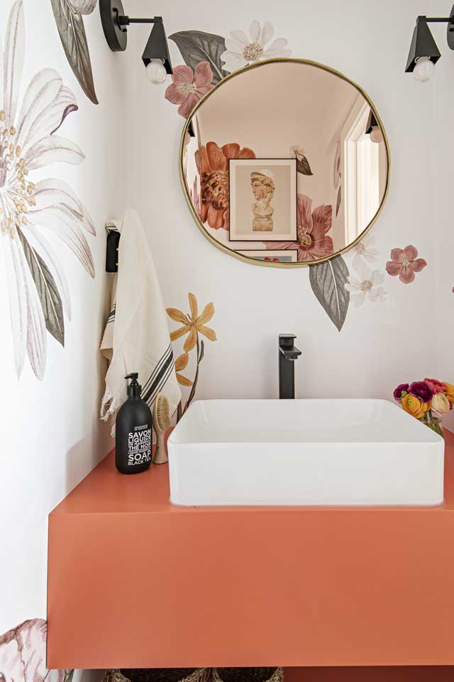 floral wallpapered bathroom with orange vanity and gold mirror